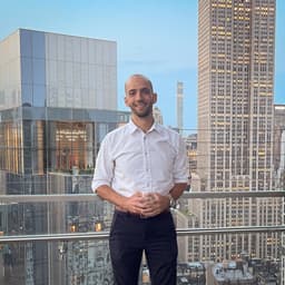 Joel Colucci standing on a terrace with the city skyline behind him.
